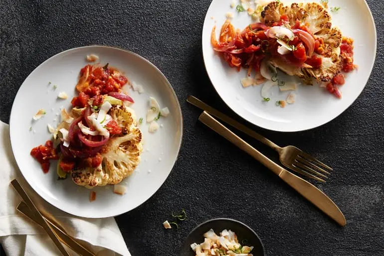 Overhead view of roasted cauliflower steaks made with Muir Glen Organic Diced Tomatoes topped with tomato chutney, coconut flakes and red onion.