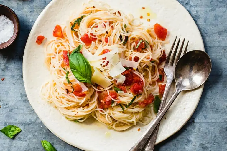 Overhead view of angel hair pasta topped with Muir Glen Organic Fire Roasted Diced Tomatoes, basil, and Parmesan cheese.