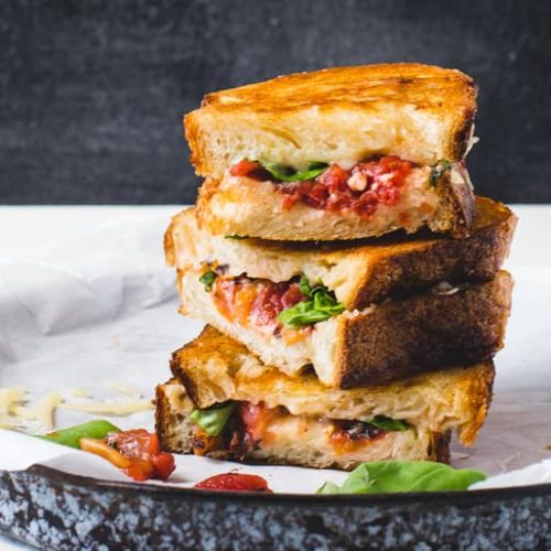 A stack of 3 grilled cheddar cheese sandwiches made from Muir Glen Fire Roasted Diced Tomatoes and basil on a platter.