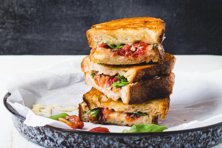 A stack of 3 grilled cheddar cheese sandwiches made from Muir Glen Fire Roasted Diced Tomatoes and basil on a platter.
