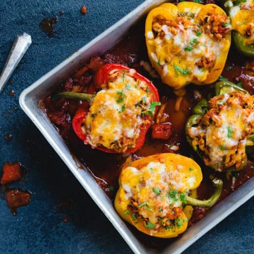 A dish of tri colored stuffed bell peppers topped with cheese