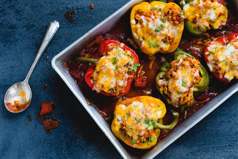 A dish of tri colored stuffed bell peppers topped with cheese