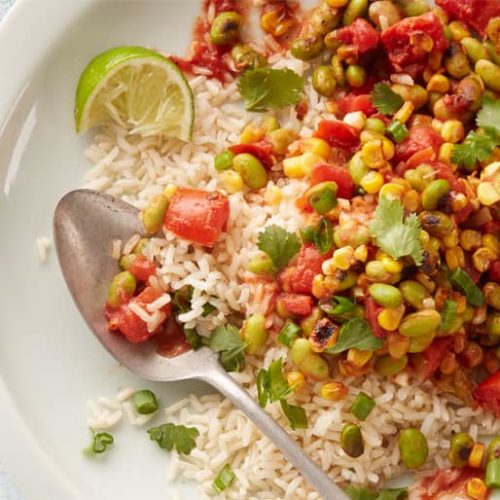 Overhead view of a plate of rice topped with vegan summer succotash made with Muir Glen Fire Roasted Diced Tomatoes.