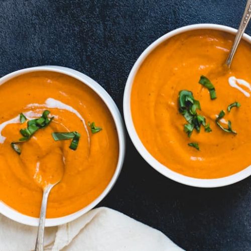 Two bowls of creamy fire roasted tomato coconut soup garnished with herbs