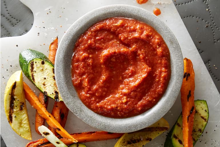Bowl of smoky romesco sauce next to grilled mixed vegetables