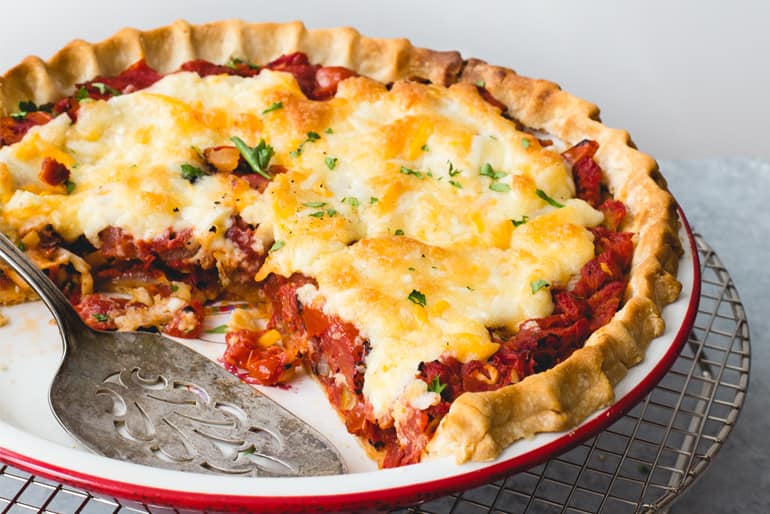 A tomato pie made with Muir Glen diced tomatoes topped with grated Parmesan cheese in a dish with a serving spoon.