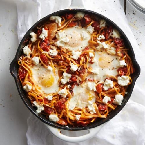 Skillet of spaghetti topped with tomato pasta sauce, four eggs and crumbled cheese