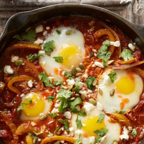 Overhead view of a skillet of Tex Mex shakshuka made with Muir Glen Medium Salsa topped with eggs, fresh herbs and queso fresco cheese.