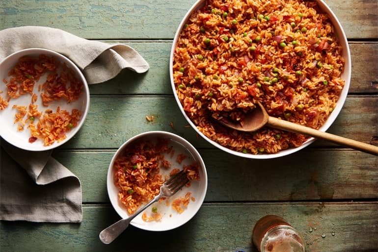 A dish of classic mexican tomato rice with a wooden spoon and two plates