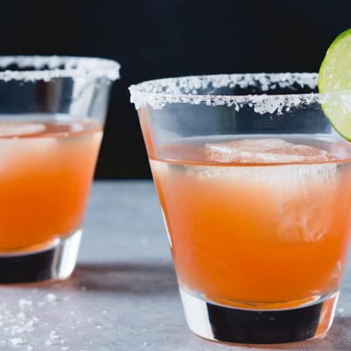 Two glasses of tomato margarita garnished with lime and salt