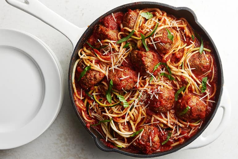 Skillet of zucchini noodles with meatballs and pasta sauce next to a plate