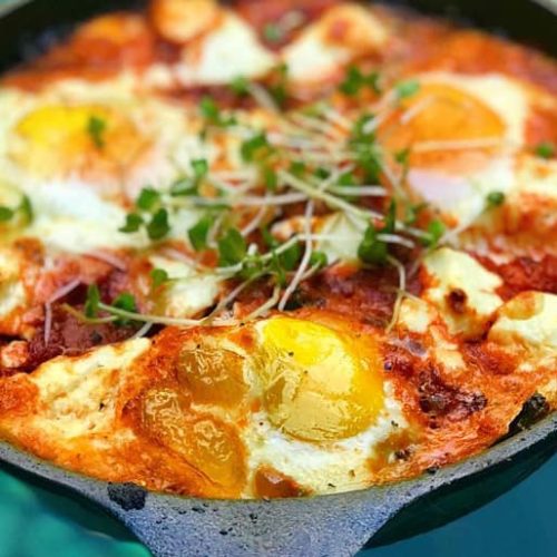 A pan of chakchouka made with Muir Glen Organic Tomato Basil Pasta Sauce topped with eggs and cress.