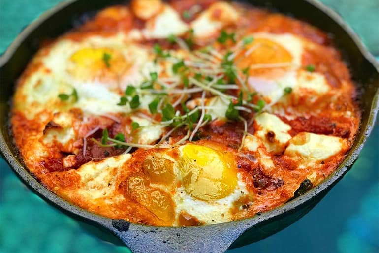 A pan of chakchouka topped with eggs and cress