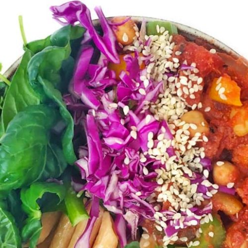 A bowl of roasted tomato and chickpea stew topped with spinach, red cabbage and sesame seeds