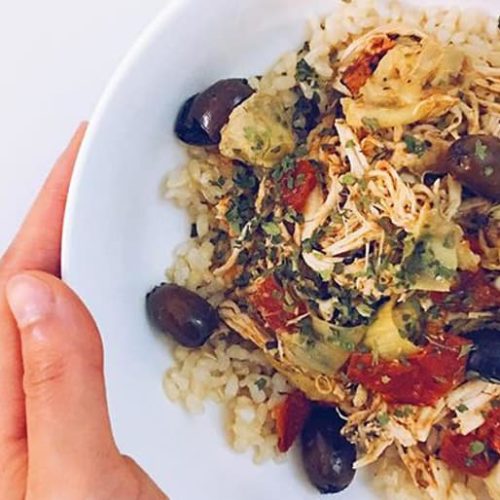 A bowl of rice topped with slow cooker mediterranean chicken, black olives and herbs