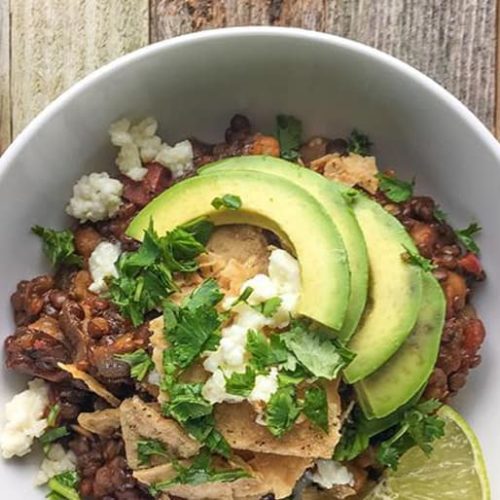 Beer lentil chili in a bowl made with Muir Glen Fire Roasted Diced Tomatoes topped with tortilla chips, avocado, lime, cotija cheese and cilantro.