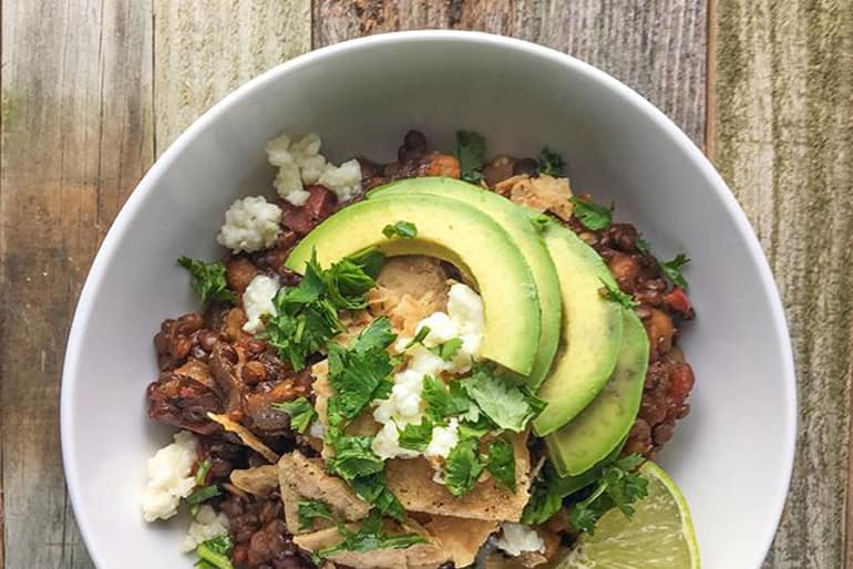 Lentil chili topped with tortilla chips, avocado, lime, cotija cheese and cilantro