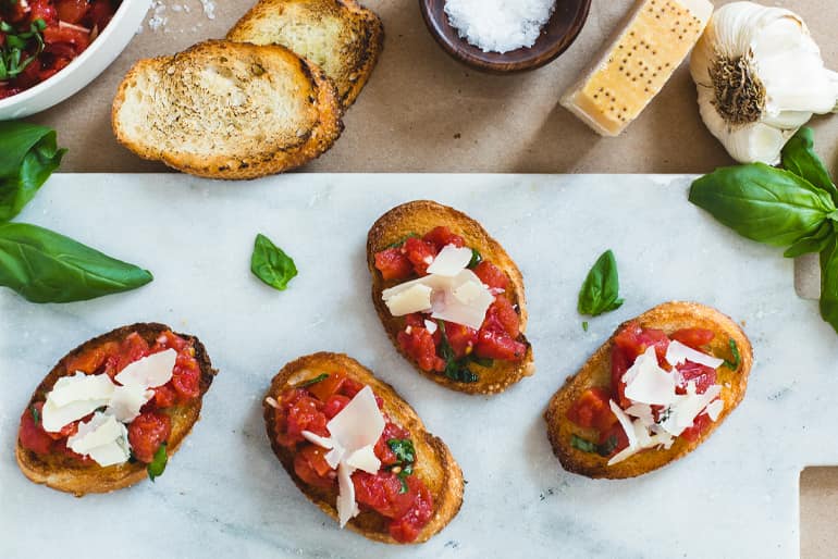 Bruschetta topped with Muir Glen Fire Roasted Diced Tomatoes, parmesan and basil on a marble surface.