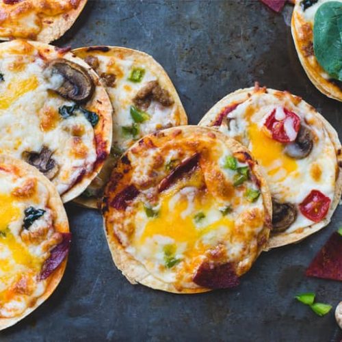 Mini pizzas topped with cheese, mushroom, tomato and salami