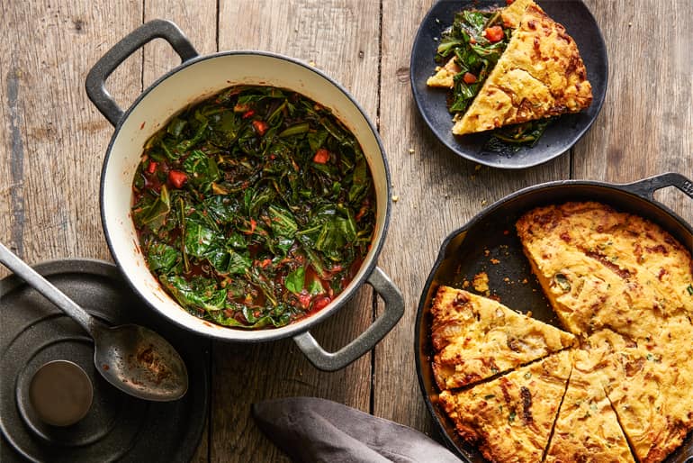 A pot of braised greens made with Glen Crushed Arabella Select Tomatoes next to a skillet of cheesy corn bread.