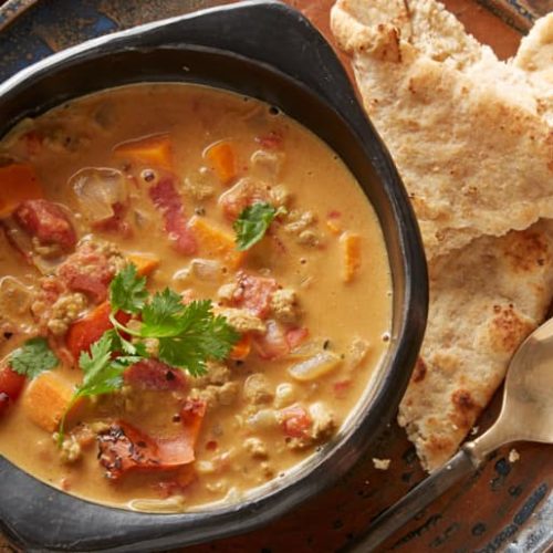 A bowl of African peanut soup made with Muir Glen Fire Roasted Diced Tomatoes topped with cilantro next to two pieces of bread and a spoon.