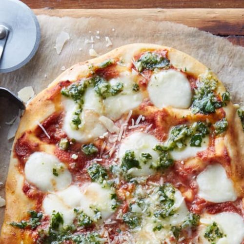 Pesto margherita pizza next to a pizza wheel