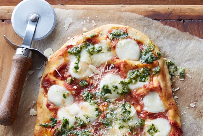 Pesto margherita pizza next to a pizza wheel