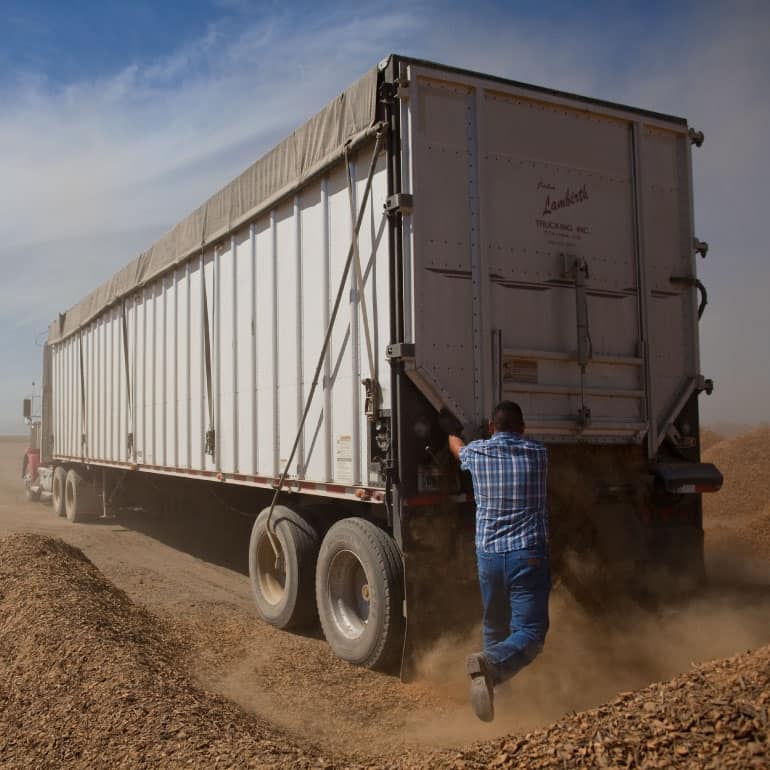 A man working on the back of a semi truck trailer on a dusty farm.