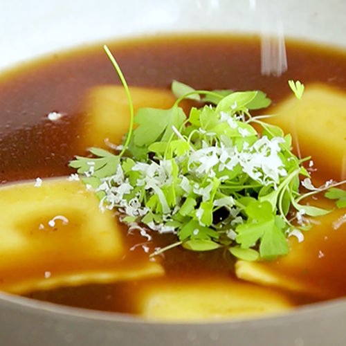 A bowl of beef bone broth with ravioli made with Muir Glen Tomato Paste and garnished with cilantro and parmesan.