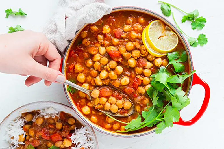 Overhead view of a bowl of chana masala made with Muir Glen Diced Tomatoes, chickpeas, herbs, and garnished with lemon.