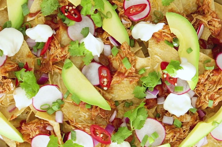 Chicken nachos made with Muir Glen Crushed Fire Roasted Tomatoes topped with avocado, sour cream, and cilantro.