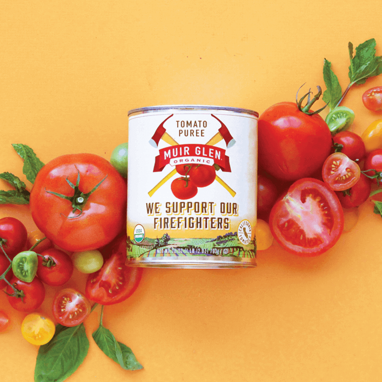Can of Muir Glen tomato puree surrounded by fresh tomatoes and herbs